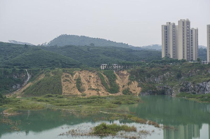 ↑6月14日，近日暴雨导致广州增城金地花园上城一栋别墅旁山体滑坡。从采石场往发生滑坡的位置看，滑坡位置在黄土上，而两旁的悬崖是石壁。据采石场的工人介绍，黄土是楼盘建设初期施工方往该处倾倒的。南都记者梁炜培摄