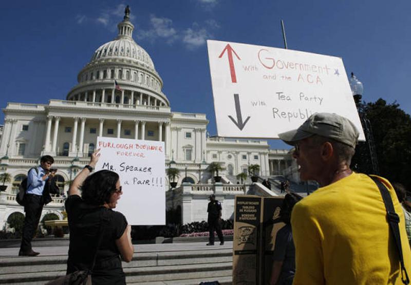2013年10月2日，在美国首都华盛顿，民众在国会大厦前举着标语抗议政府关门。
