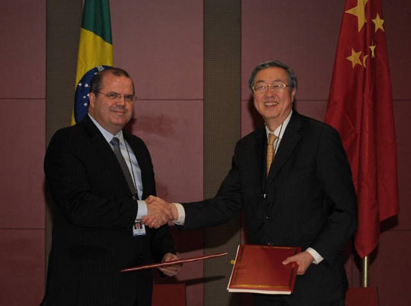 2013年3月26日，在南非德班，中国人民银行行长周小川（右）与时任巴西中央银行行长亚历山大·通比尼在签署了中巴双边本币互换协议后握手合影。