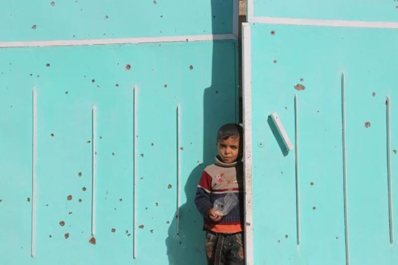 ↑ 11月20日，在伊拉克北部城市摩苏尔，一名儿童站在家门口，门上有许多弹孔，以及汽车炸弹爆炸后留下的痕迹。 新华社记者刘万利摄