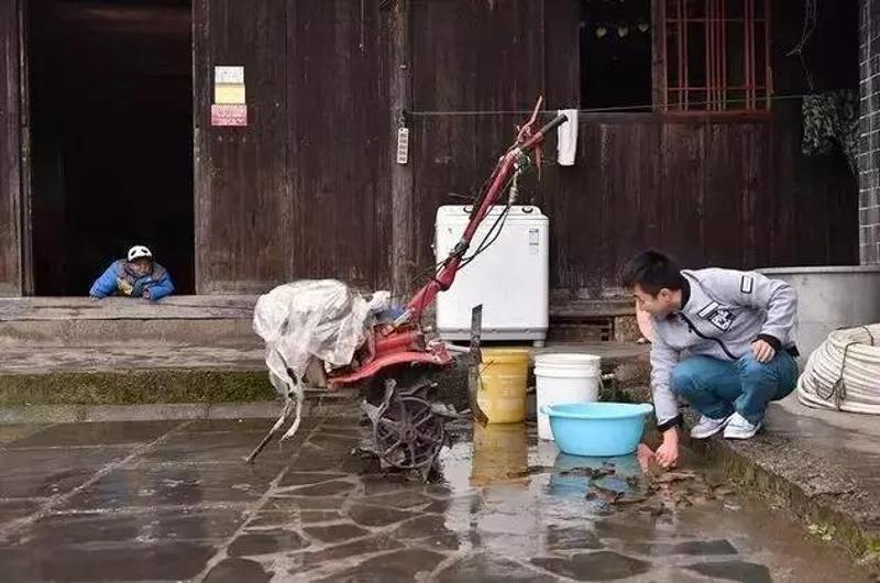 ▲石欣在屋外冲洗自家养的黄鳝，儿子趴在门槛上叫爸爸。