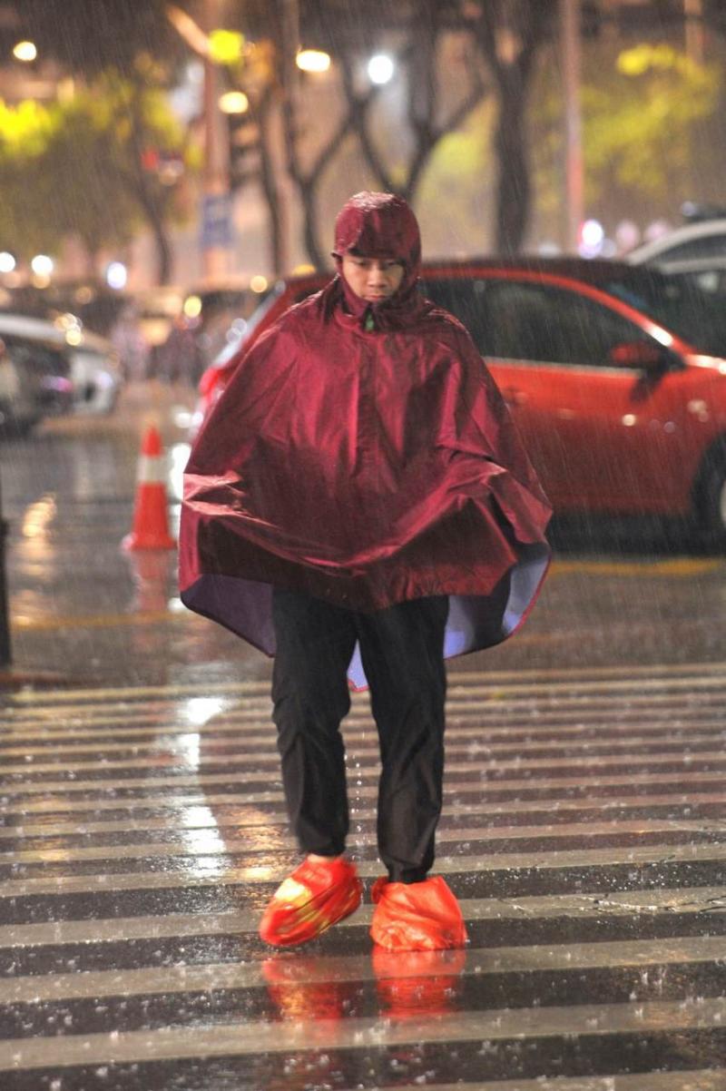 佛山街头,一市民穿着雨衣,脚上套着塑料袋在雨中前行(摄影/戴嘉信)